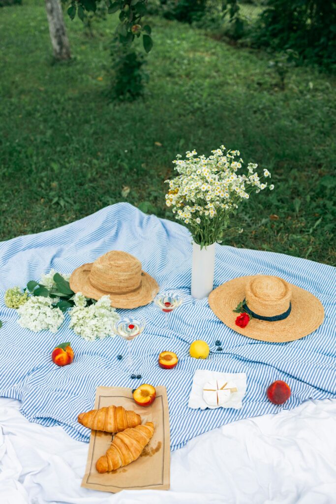 A picnic rug laid out with straw hats, flowers and fruit.